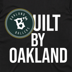 On a black background, bold white text displays "Built By Oakland." A circular logo featuring "Oakland Ballers" encircling a stylized "B," bordered in green and white, overlaps the design. To explore the exclusive Built By Oakland owner's t-shirt, reach out to investors@oaklandballers.com.